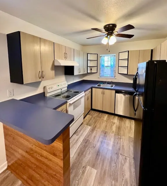 Wood-finish flooring, light wood-finish cabinetry, blue countertops, and ceiling fan with integrated lighting
