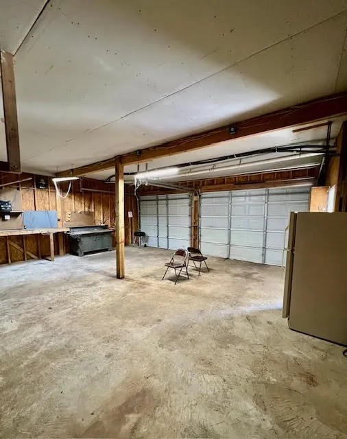Spacious garage with exposed beam ceiling, concrete flooring, and two overhead doors