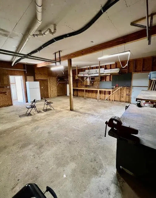 Spacious utility area featuring exposed wood beam construction, concrete flooring, fluorescent lighting, and built-in shelving