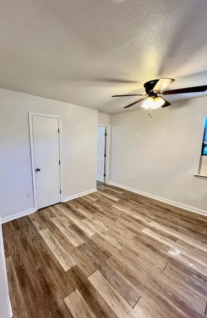 Wood-finish flooring, white walls, and a ceiling fan with integrated lighting