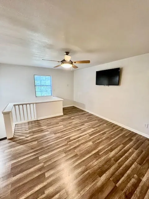 Wood-finish flooring, ceiling fan with integrated lighting, white painted walls, and an interior railing