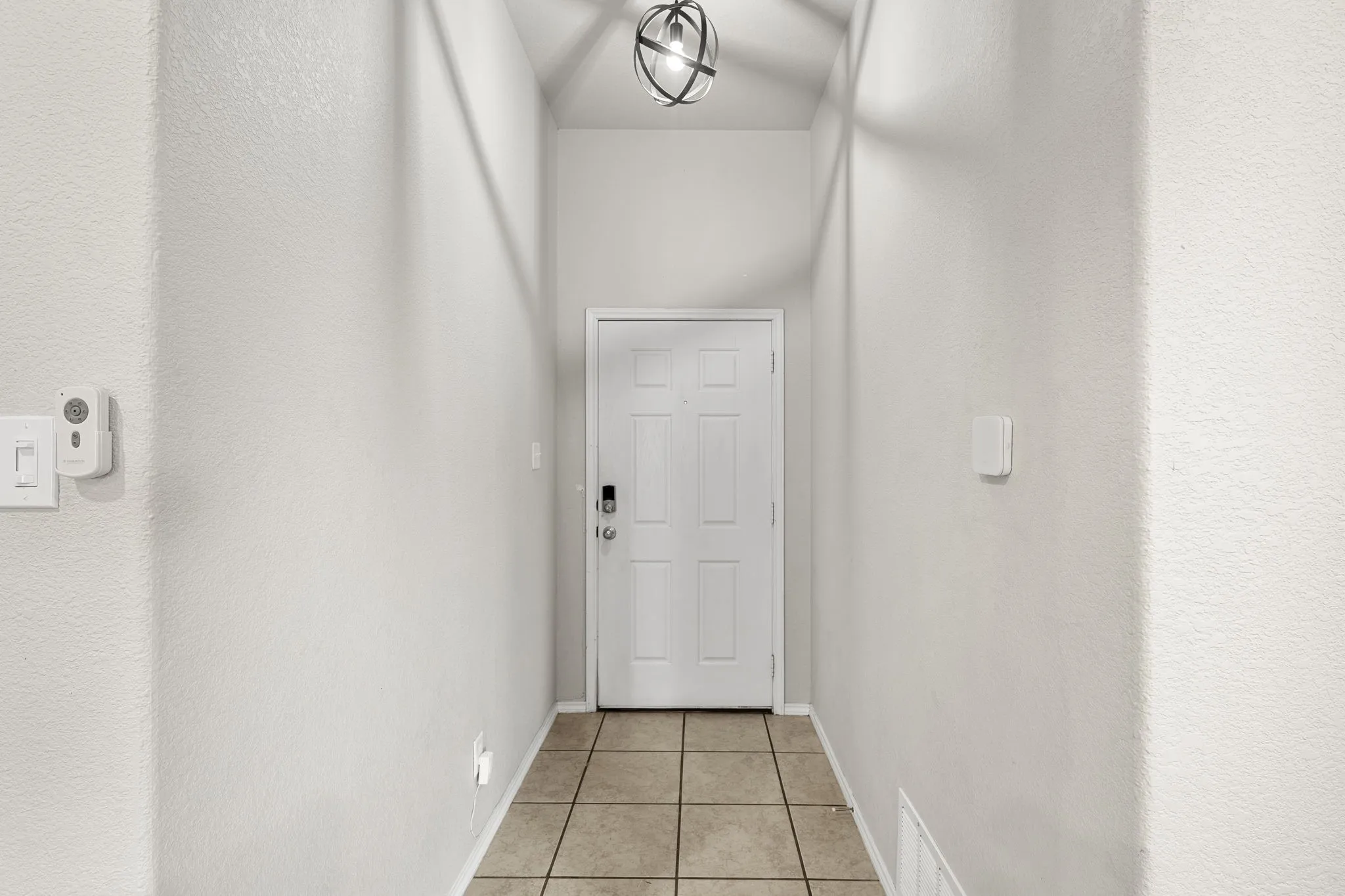 Tiled flooring leading to a paneled entry door with a smart lock