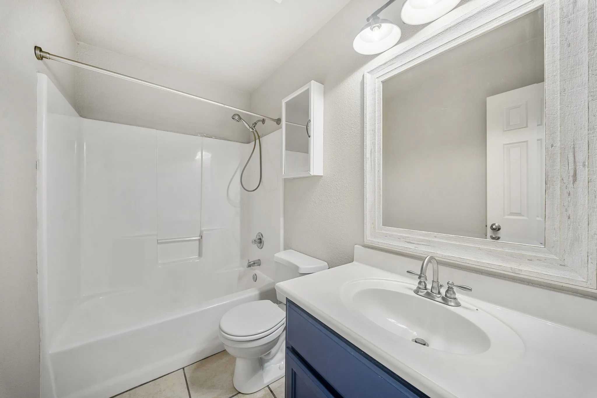 White shower/tub combination, single vanity with integrated sink, wood-finish mirror, and overhead vanity lighting