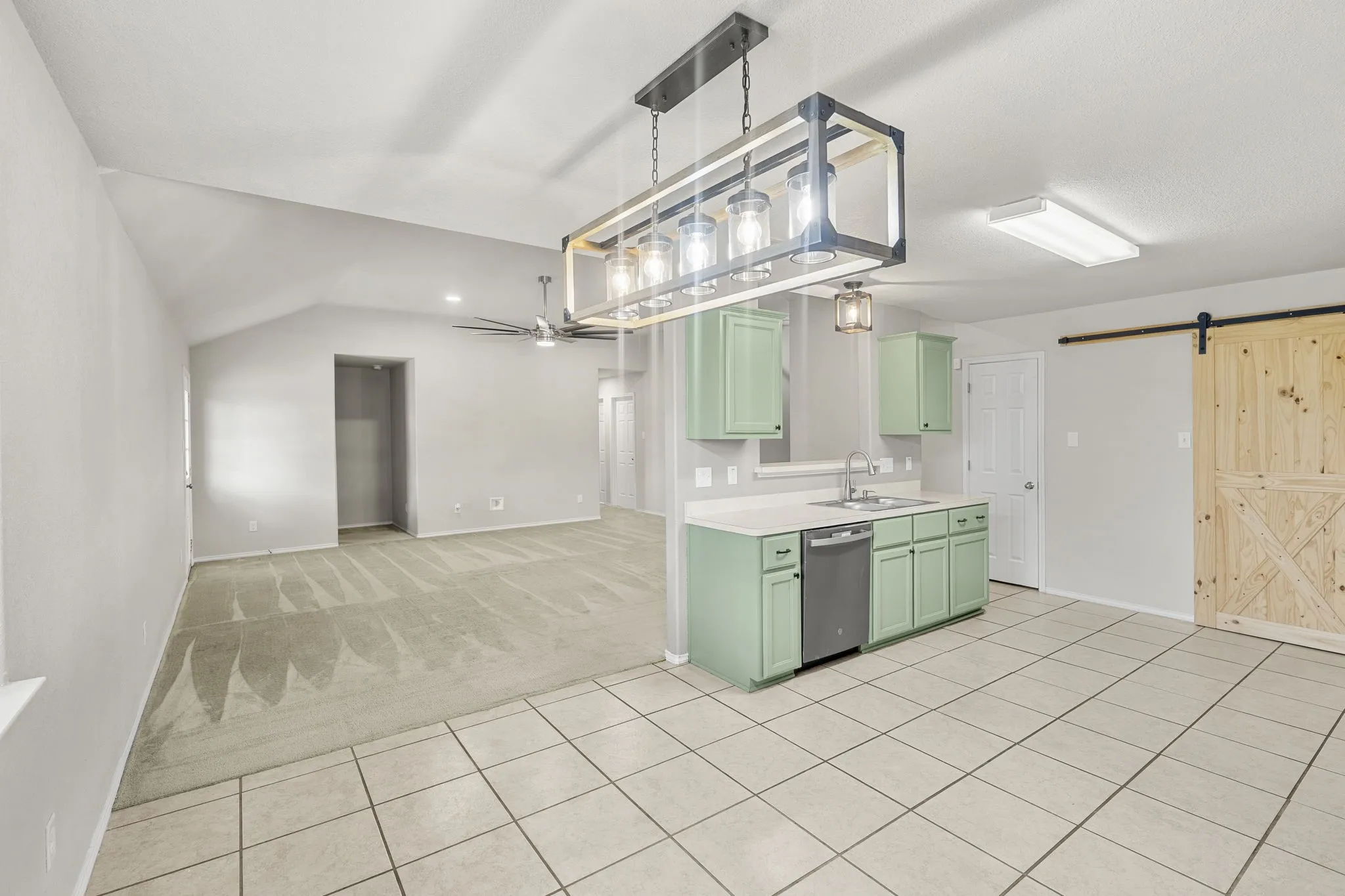 Vaulted ceiling, ceiling fan, tile flooring, light green cabinetry, and a wood-finish barn door