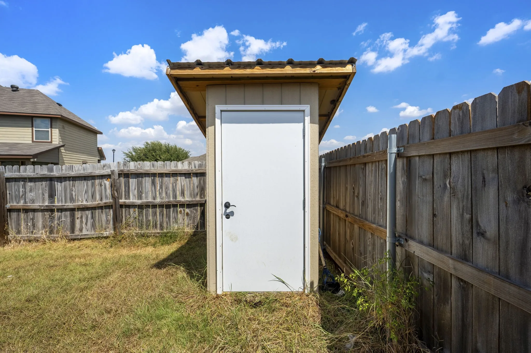 Detached storage shed featuring a white door and an asphalt shingle roof