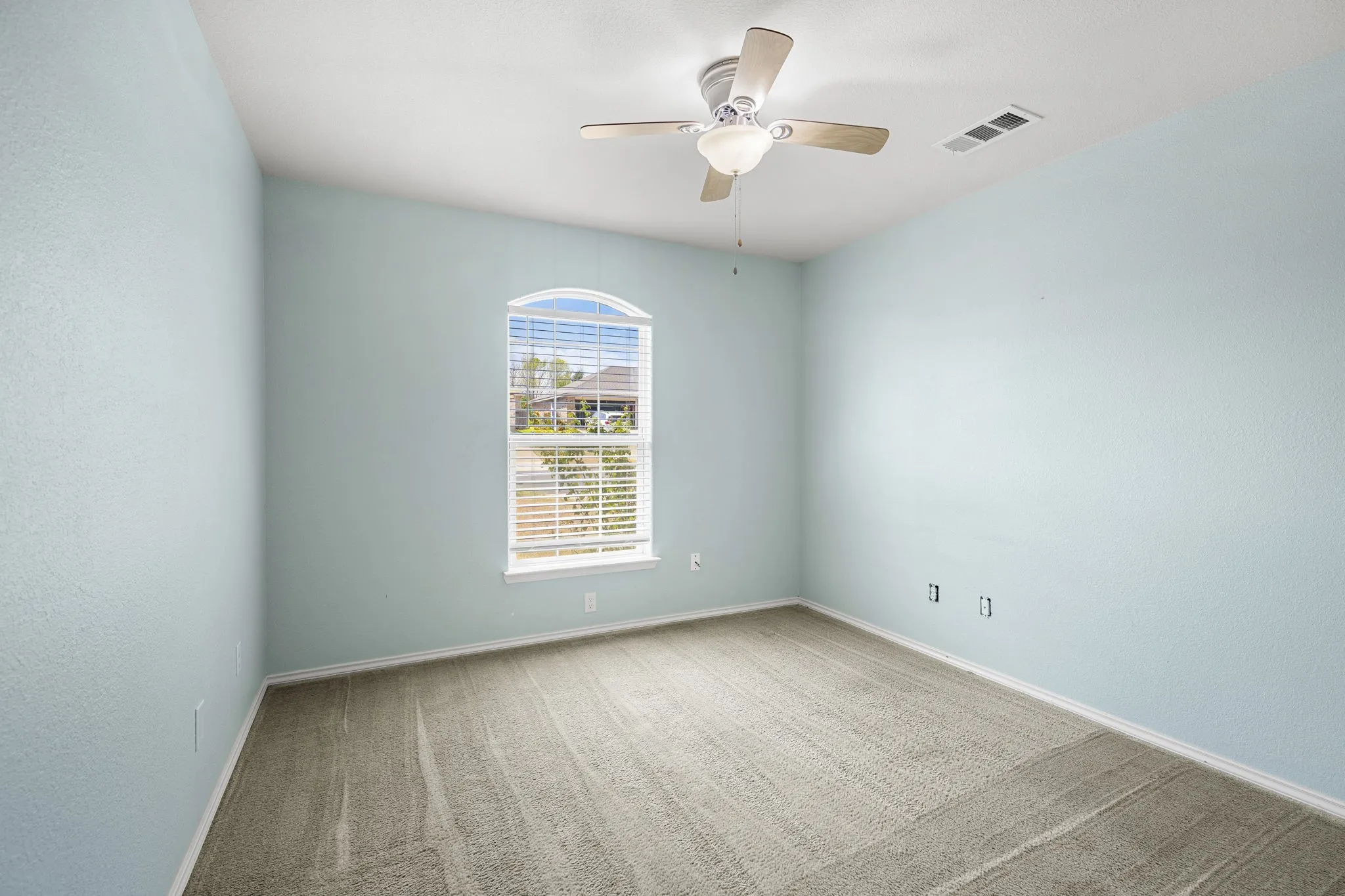 Arched window with blinds, ceiling fan, and light blue wall finish