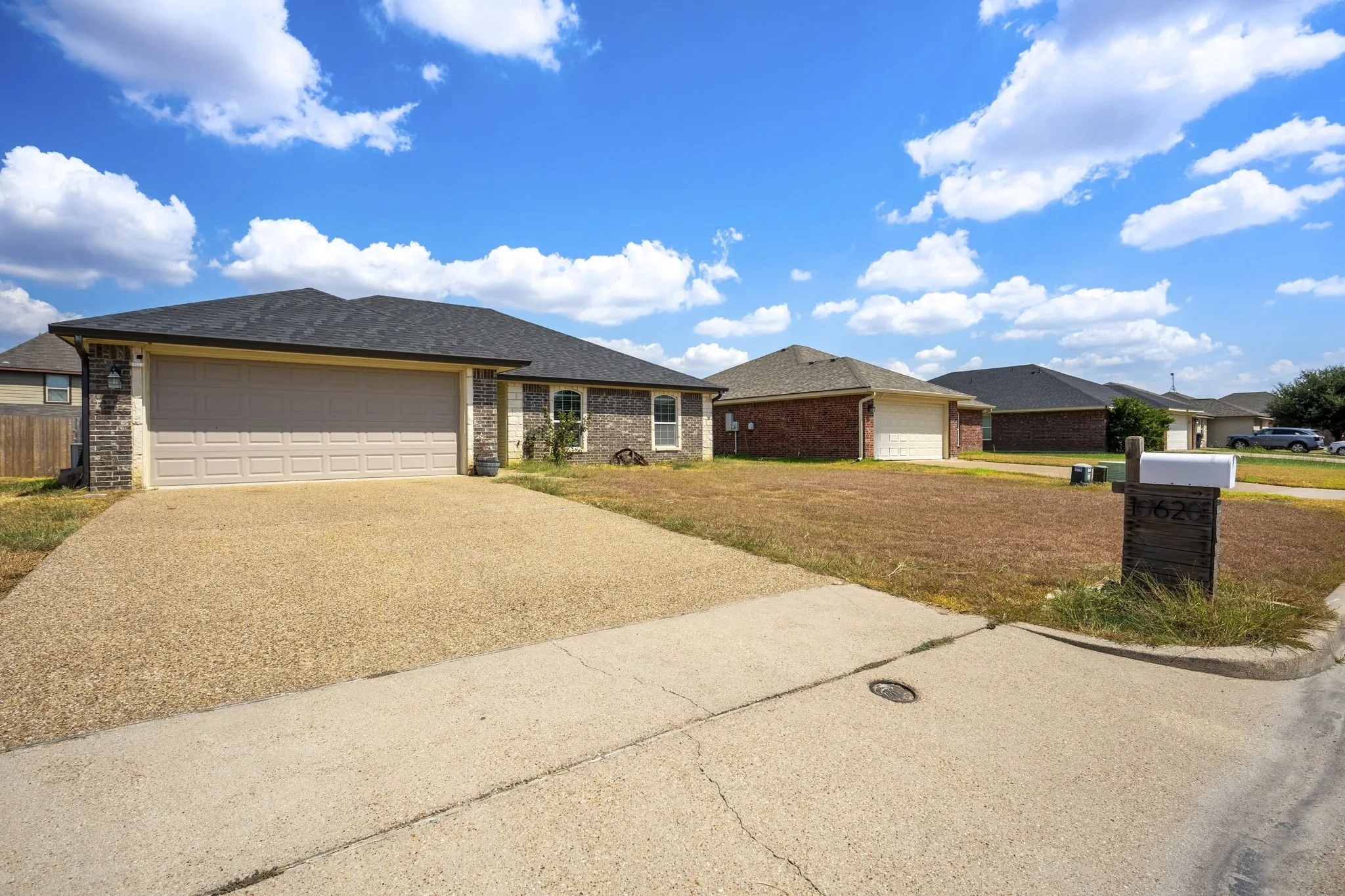 Brick and stone veneer exterior with a two-car garage, shingle roof, and an exposed aggregate driveway