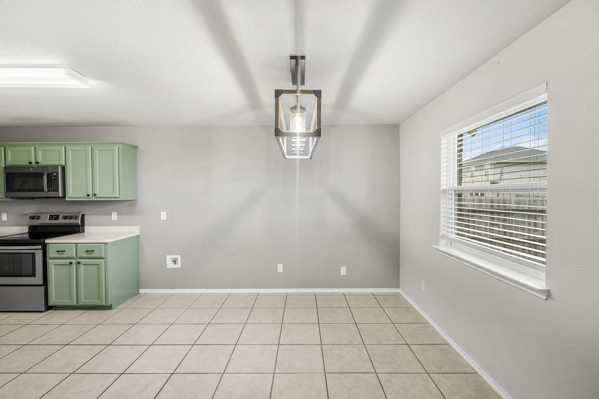 Kitchen area with sage green cabinetry, stainless steel appliances, tile flooring, and a large window with blinds
