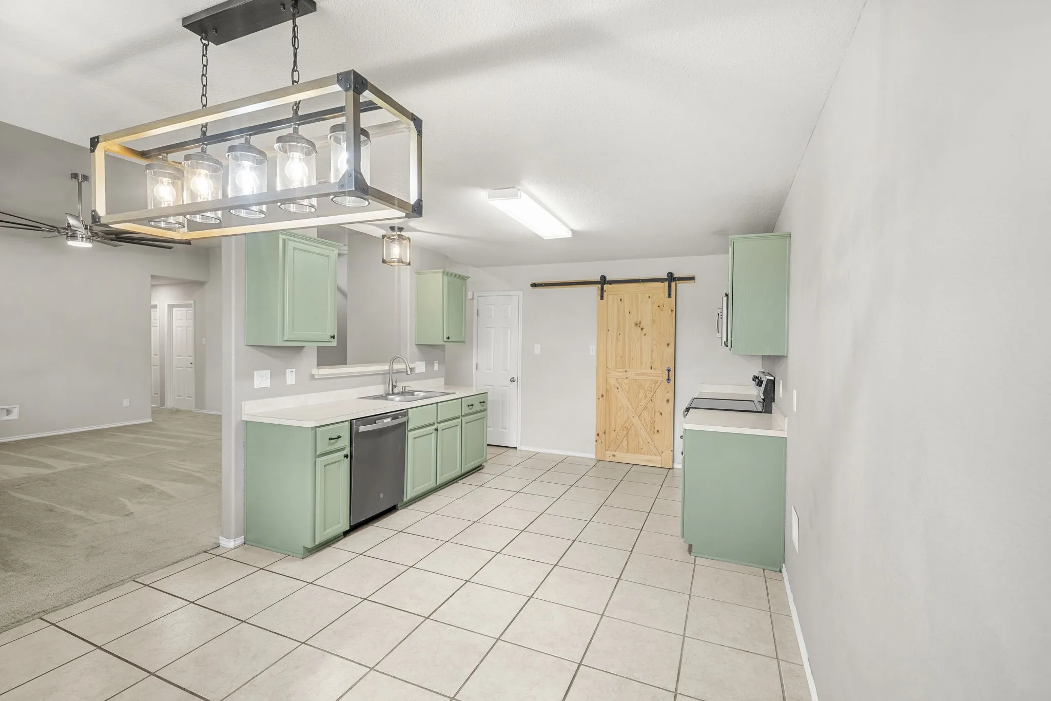 Kitchen with tile flooring, light green cabinetry, stainless steel dishwasher, white countertops, and a barn door