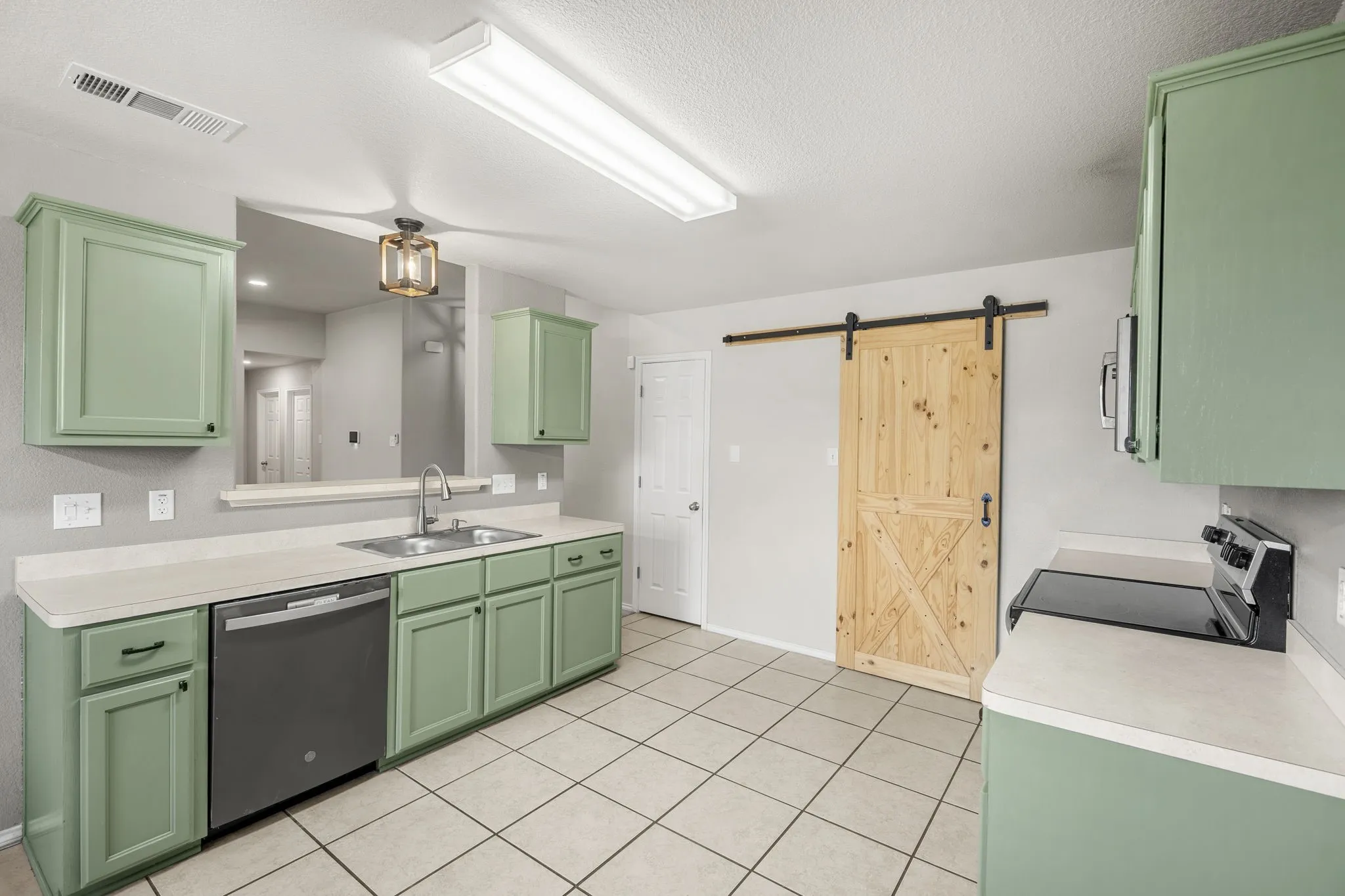 Kitchen featuring green cabinetry, light countertops, tile flooring, a stainless steel sink, and a barn door