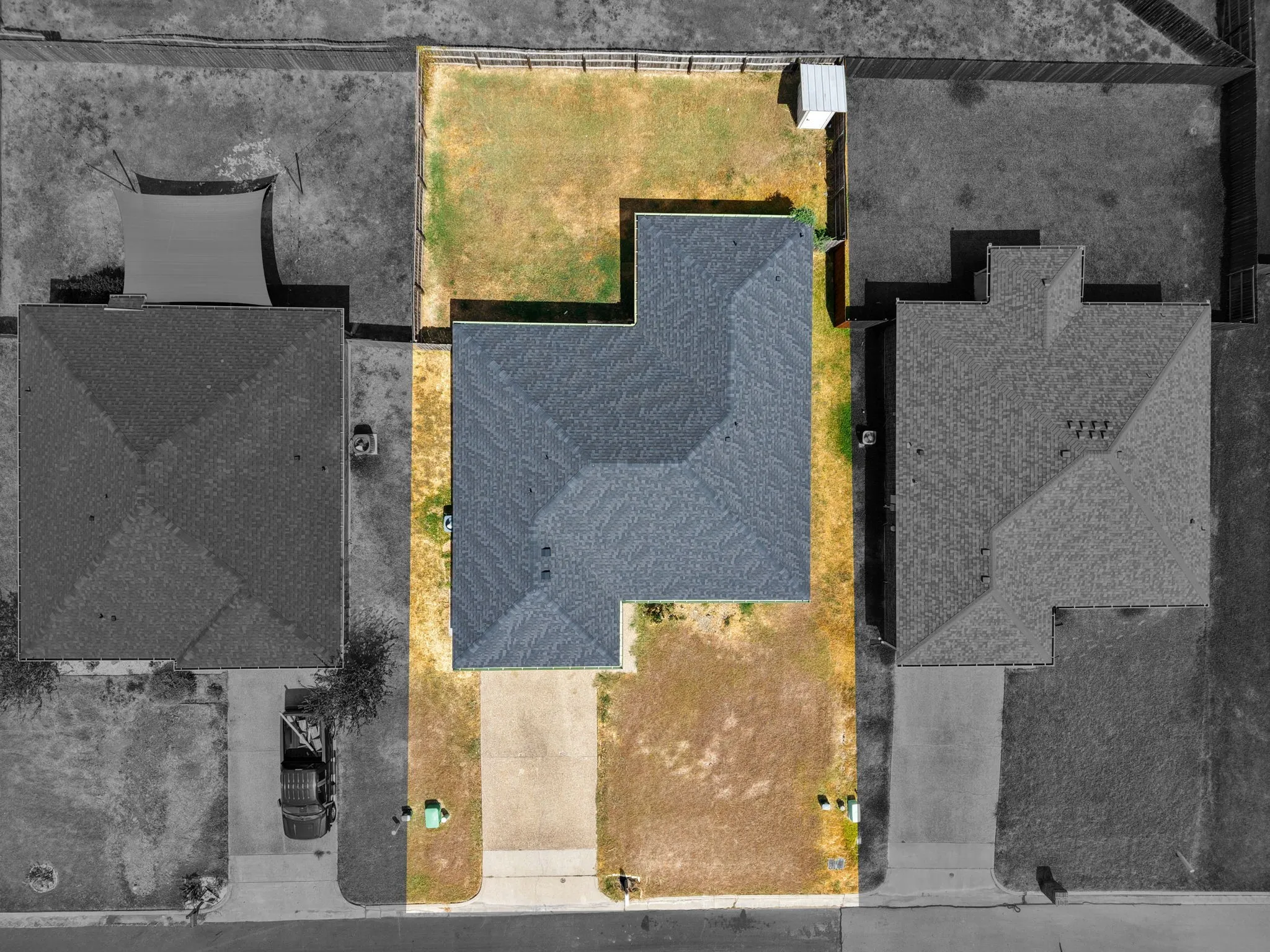 Gabled roofline, concrete driveway, fenced perimeter, and a detached shed