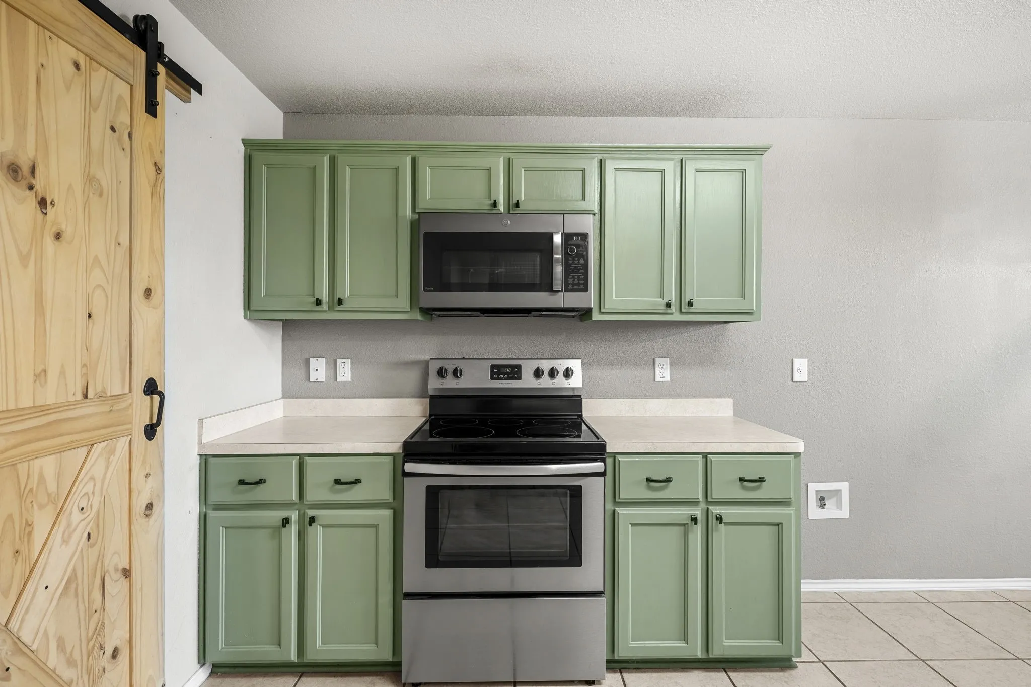 Kitchen featuring green cabinetry, light-toned countertops, stainless steel appliances, and a natural wood-finish barn door