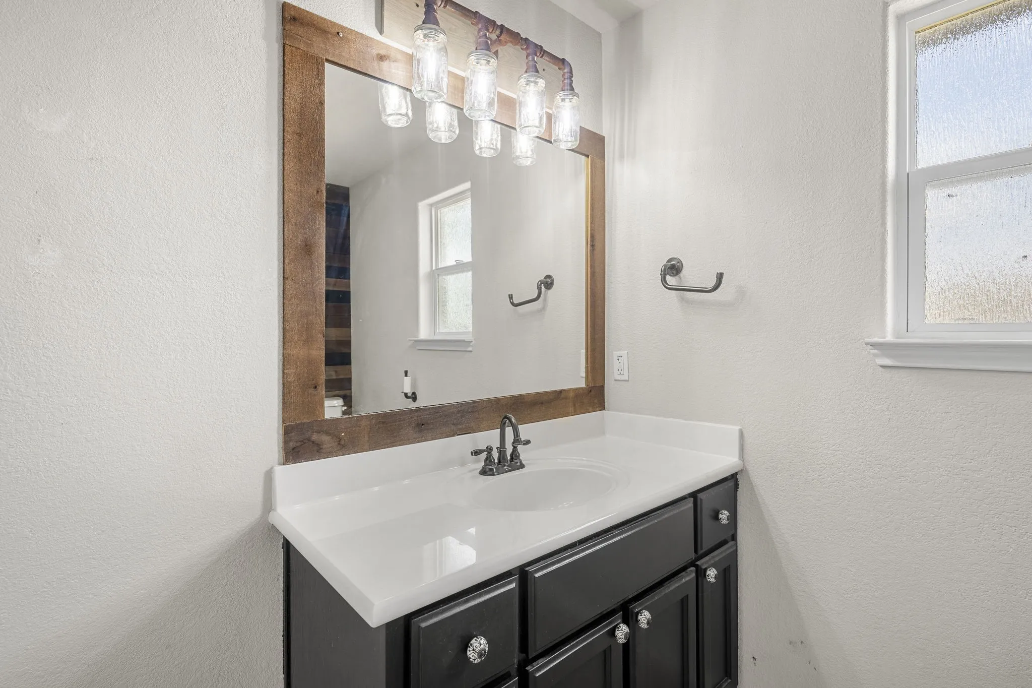 Vanity with black cabinetry, white countertop, and integrated sink