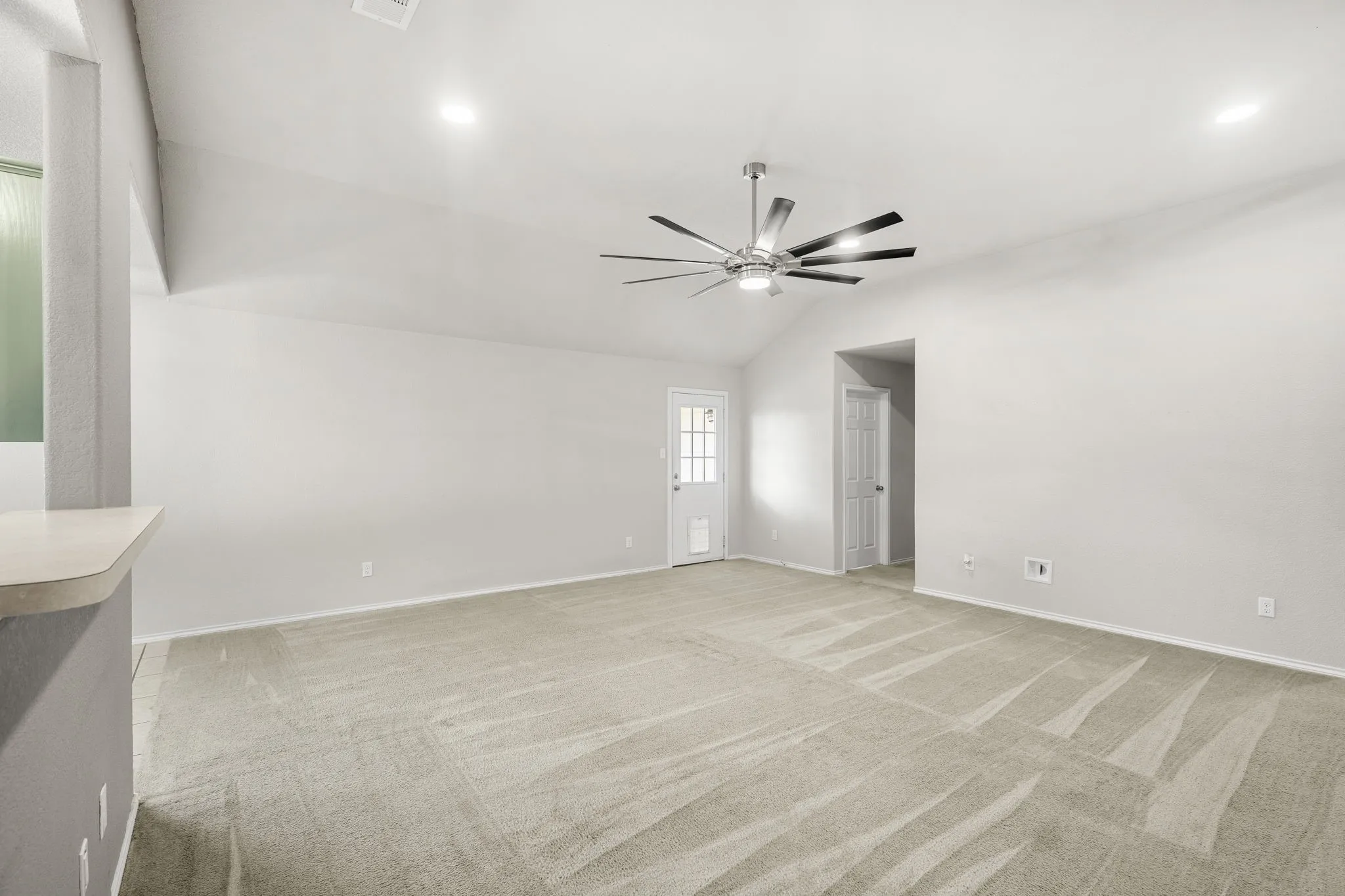 Vaulted ceiling with recessed lighting and a ceiling fan, light-colored carpeting, and a white paneled door