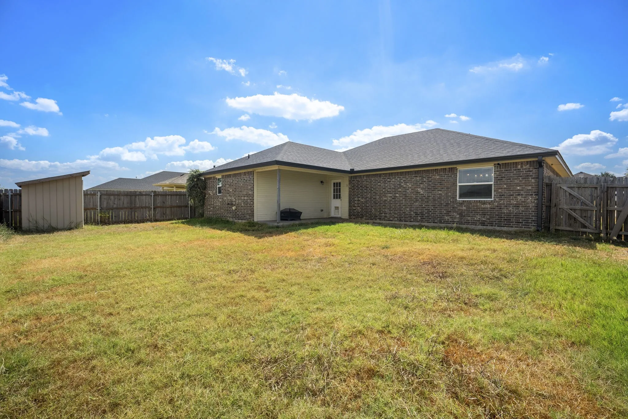 Expansive backyard with a wood privacy fence, featuring a storage shed and a covered patio area