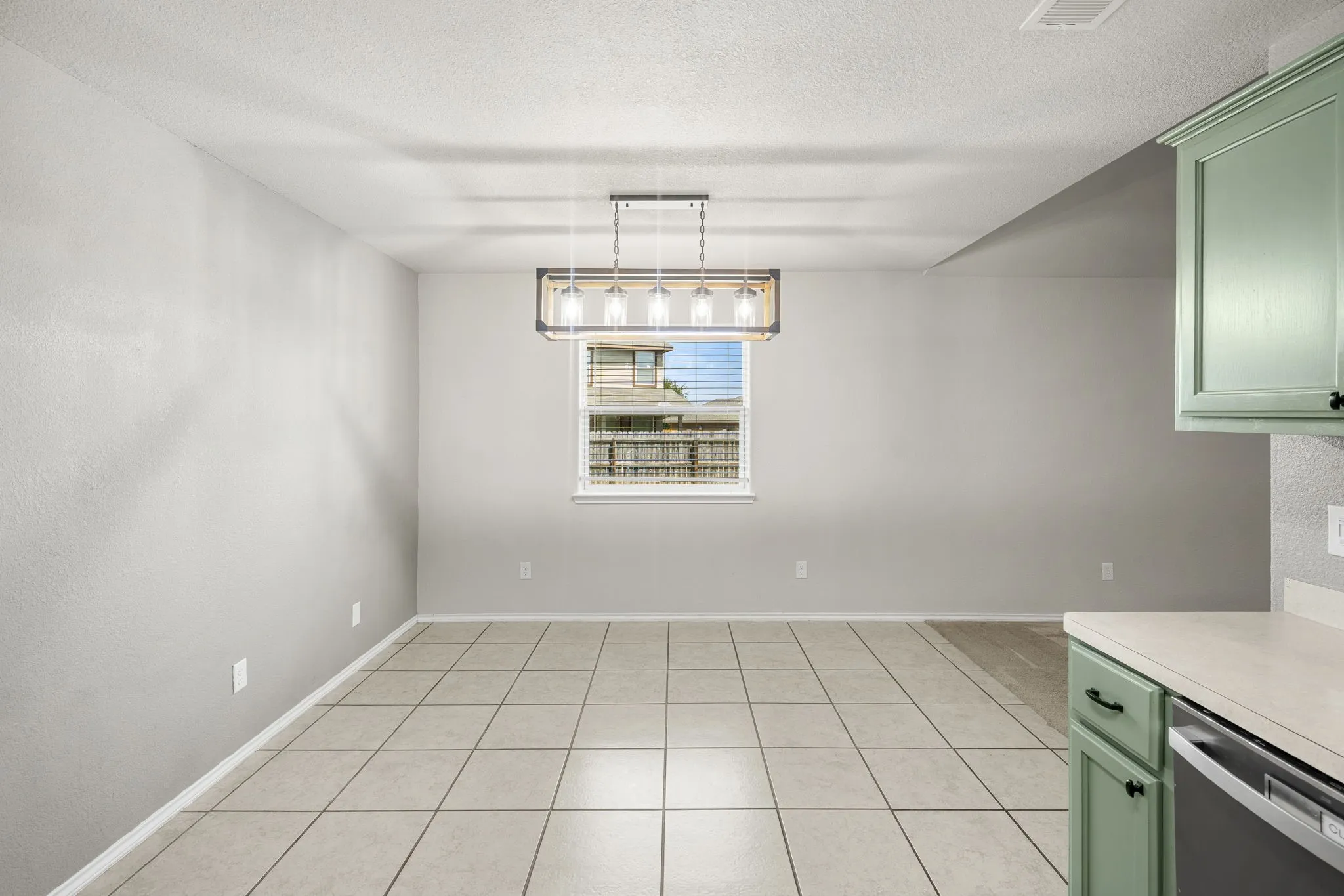 Spacious room featuring tile flooring, a window with blinds, and a multi-bulb chandelier