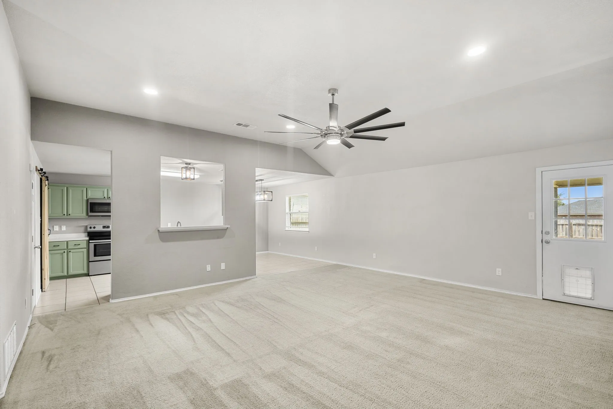 Vaulted ceiling with recessed lighting and a ceiling fan, a pass-through window to the kitchen featuring green cabinetry, and wood-finish flooring