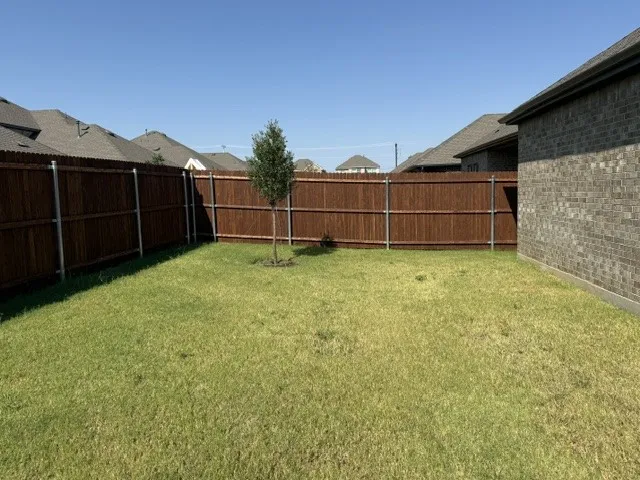 Expansive backyard featuring a manicured lawn, established privacy fencing, and brick exterior