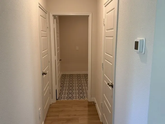Hallway featuring wood-finish flooring, paneled interior doors, and a digital thermostat