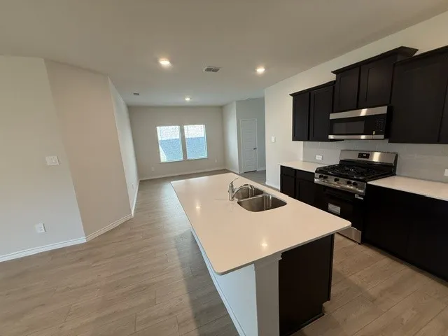 Kitchen island with dual basin sink, stainless steel appliances, dark wood-finish cabinetry, and light-toned countertops