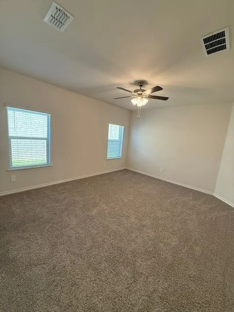 Spacious room with neutral-toned carpet, light-colored walls, multiple windows with blinds, and a ceiling fan with integrated lighting
