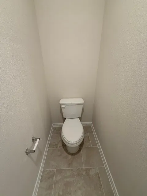 Tile flooring with white baseboards, a white two-piece toilet, and a chrome toilet paper holder