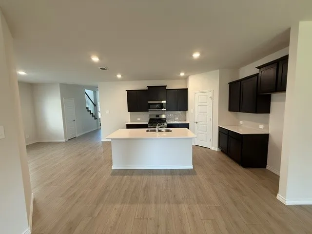 Kitchen featuring wood-finish flooring, dark cabinetry, a central island with an undermount sink, recessed lighting, and a subway tile backsplash