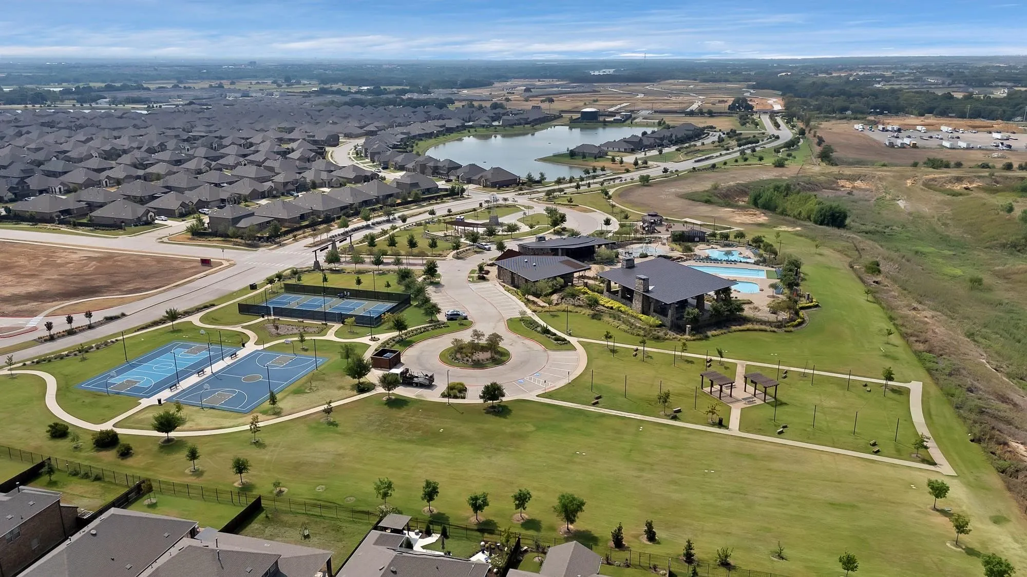 Community club building with an expansive swimming pool, multiple sports courts, and a large central lake