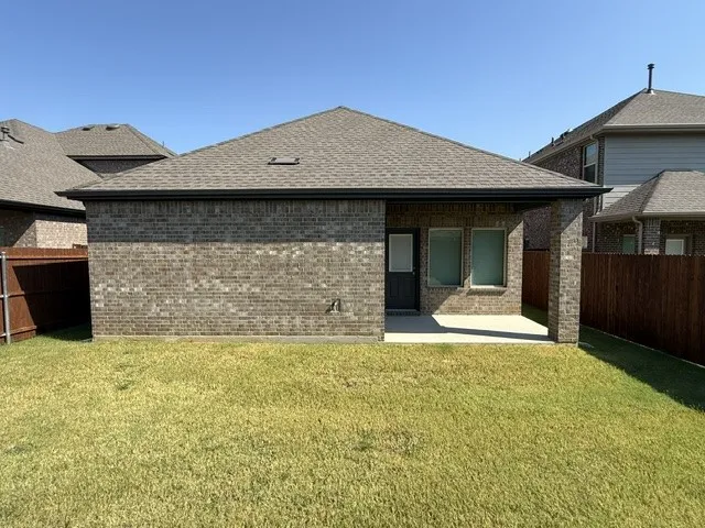 Brick exterior with a covered patio, two windows, and a wood privacy fence