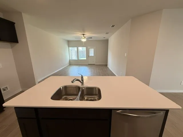 Kitchen island with a light-toned countertop, stainless steel double basin sink, and a stainless steel dishwasher