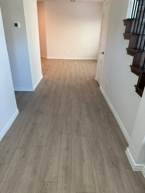 Light wood-finish flooring extending through the space, white trim, and a white interior door