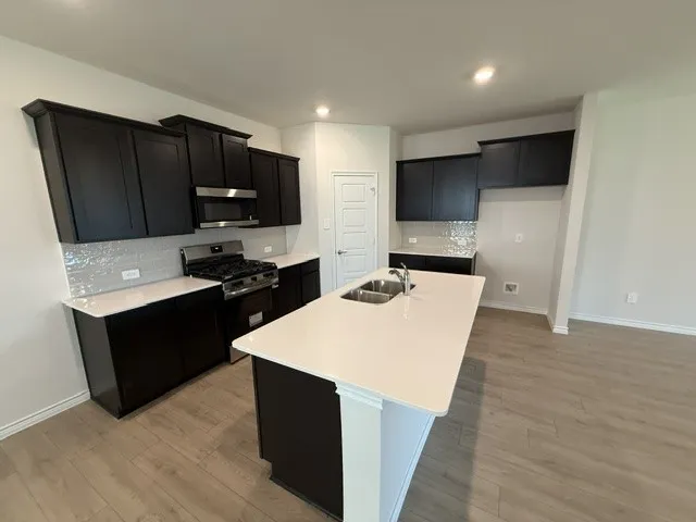 Kitchen featuring dark wood-finish cabinetry, white countertops, tile backsplash, and a central island with a double basin sink