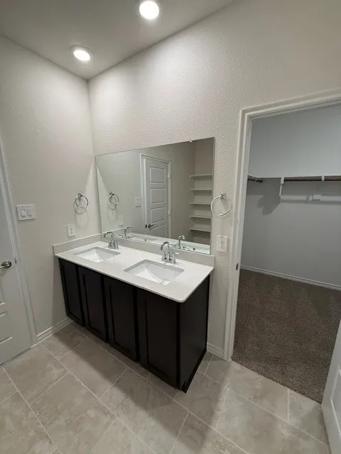 Dual vanity with integrated sinks, quartz countertop, dark wood-finish cabinetry, full-width mirror, and recessed lighting