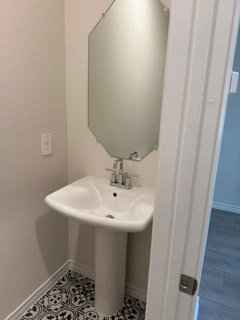 Pedestal sink, patterned floor tiles, hexagonal mirror, and white trim