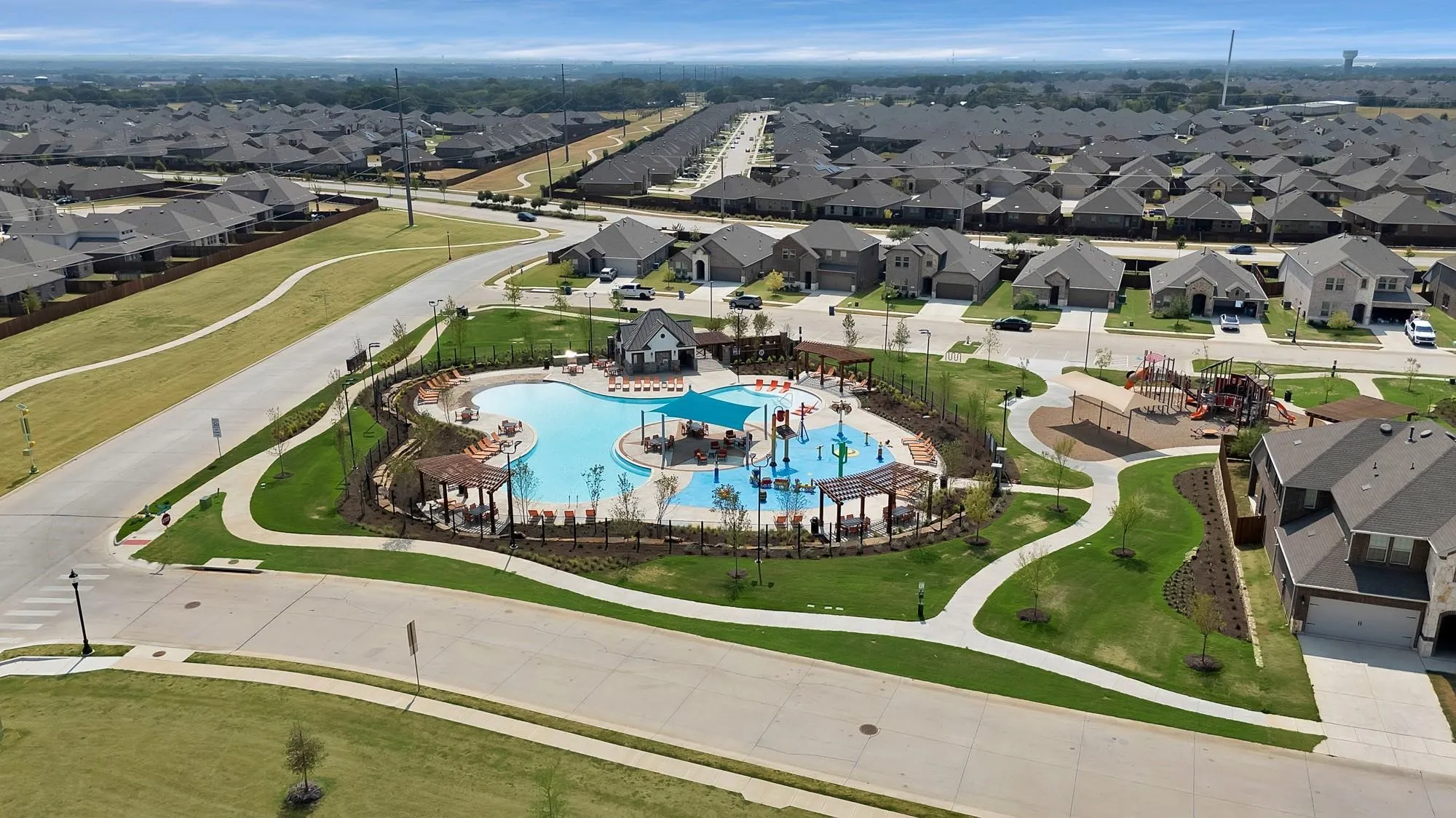 Community pool with integrated water features, shaded seating areas, and adjacent green spaces, surrounded by residential properties