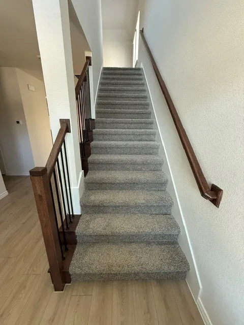 Staircase featuring wood-finish flooring, carpeted treads, wood handrails, and metal balusters