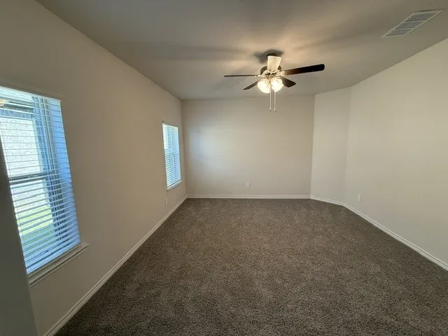 Neutral wall color, carpet flooring, multiple windows with blinds, and a ceiling fan