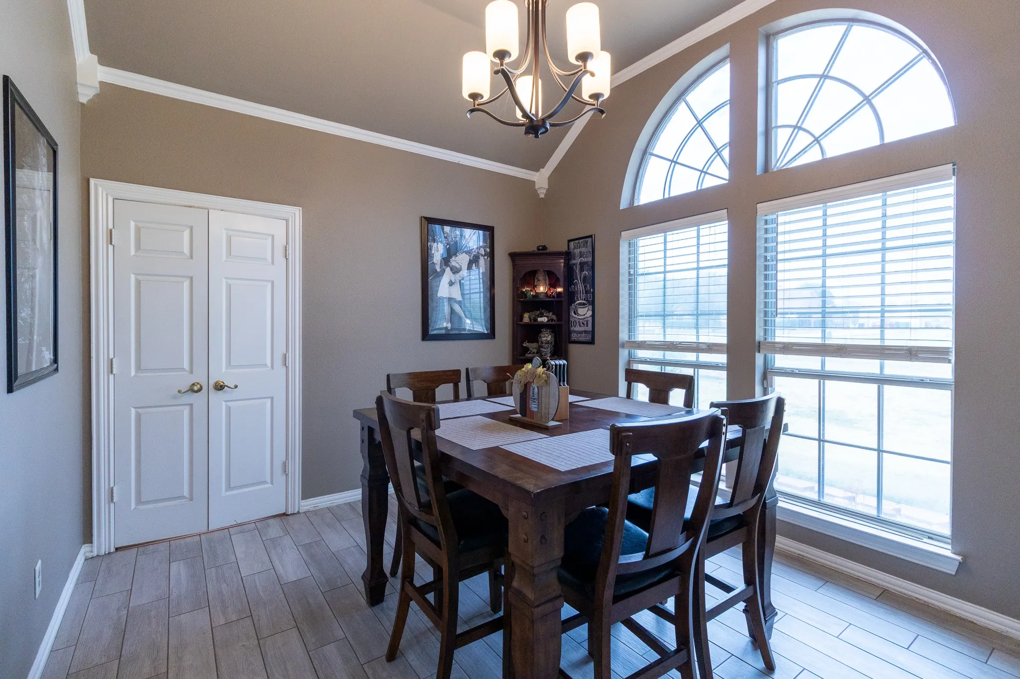 Vaulted ceiling with crown molding, arch-top window, wood-finish flooring, and recessed panel double doors