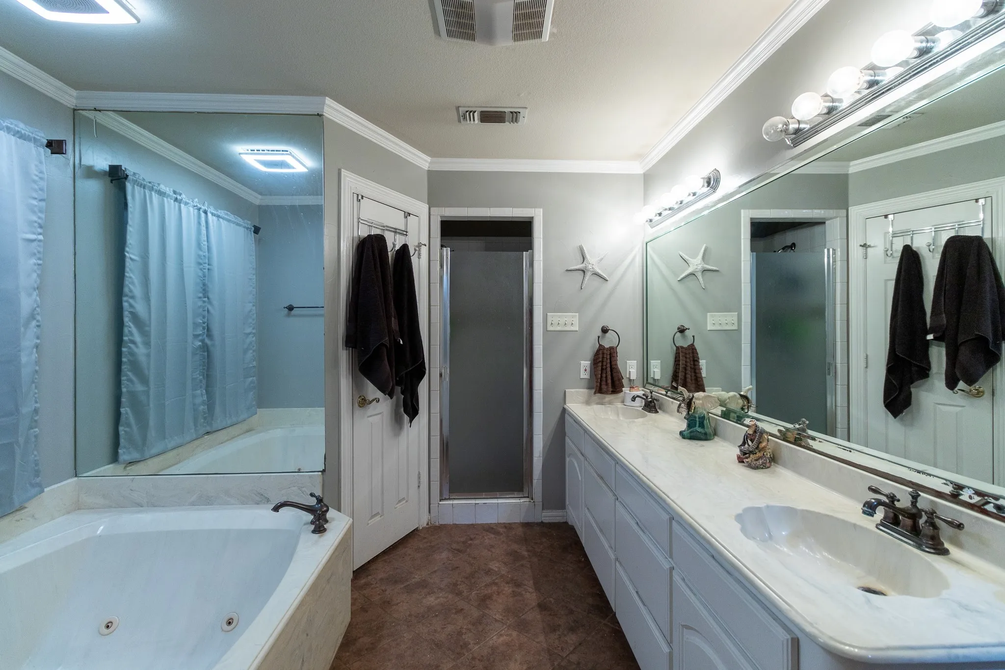 Dual vanity with integrated sinks and a large mirror, corner soaking tub with deck-mounted faucet, and a separate shower enclosure with a frosted glass door