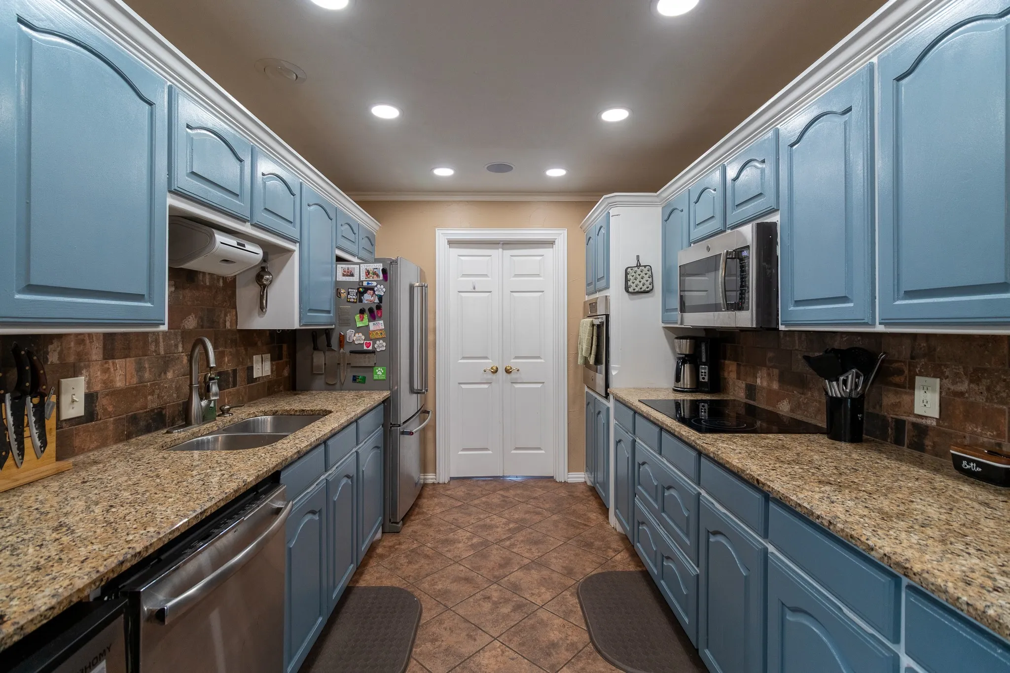 Galley kitchen featuring blue painted cabinetry, stone-look countertops, stainless steel appliances, and a tiled backsplash