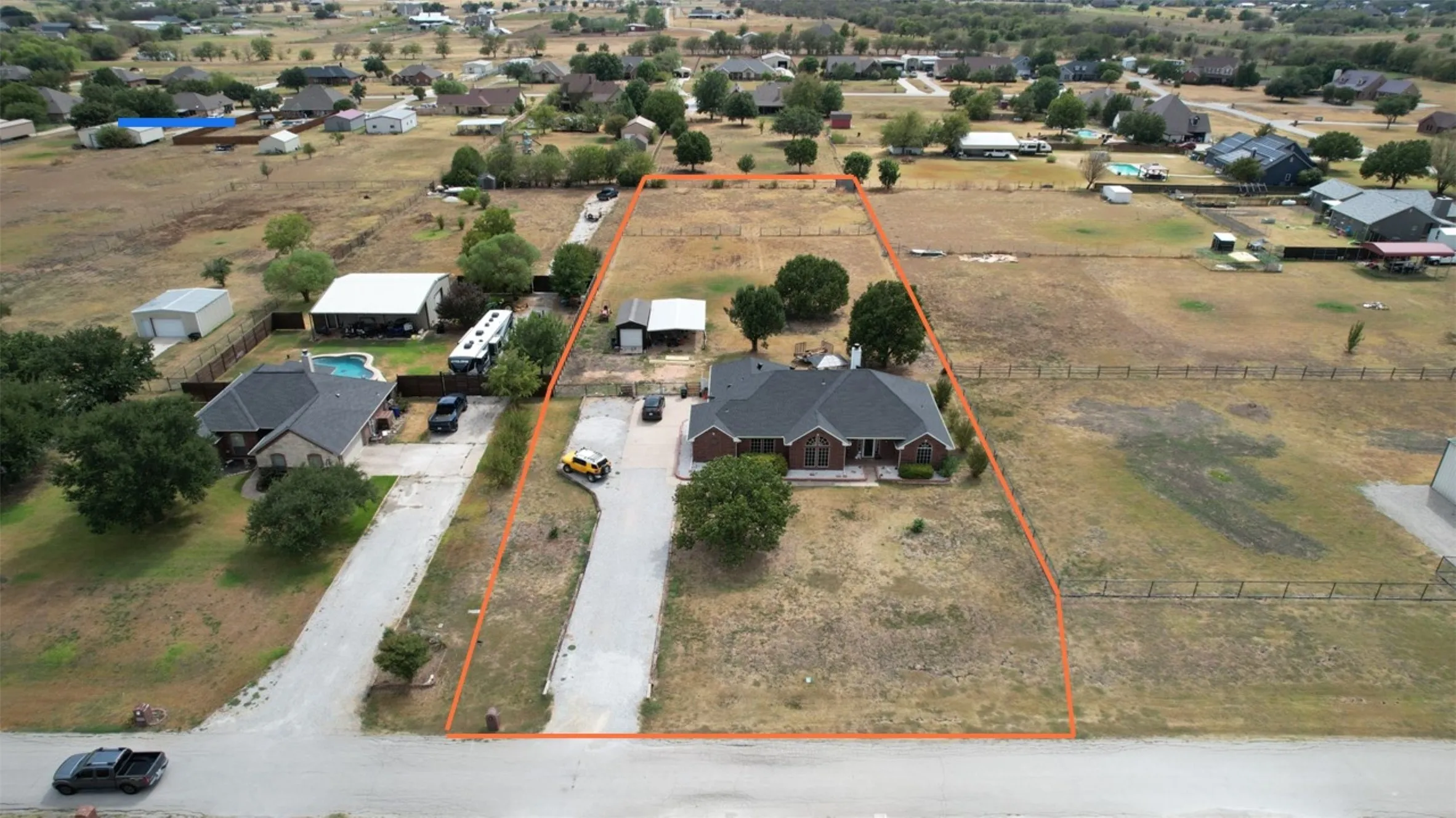 Expansive lot featuring a single-story brick residence with a dark roof, mature trees, and a long driveway