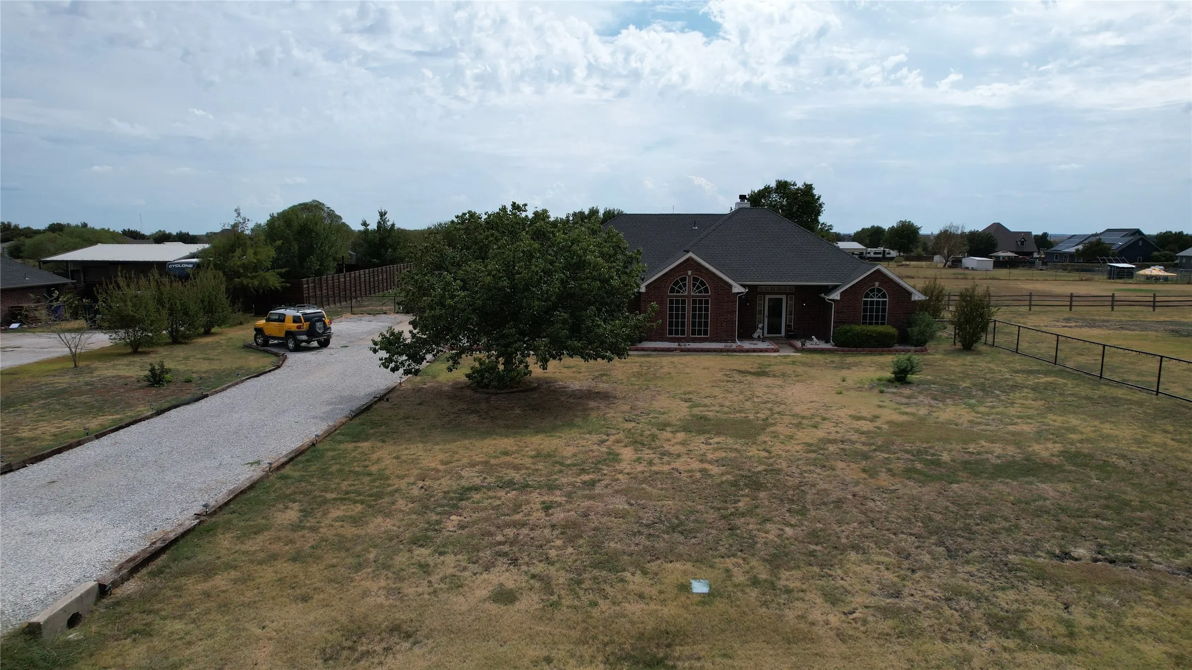 Brick exterior with arched windows, mature landscaping, and a gravel driveway