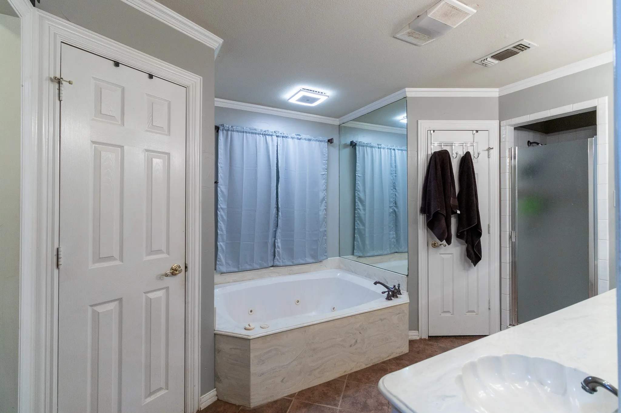 White panel doors, crown molding, built-in jetted tub, mirrored wall, and a glass-enclosed shower