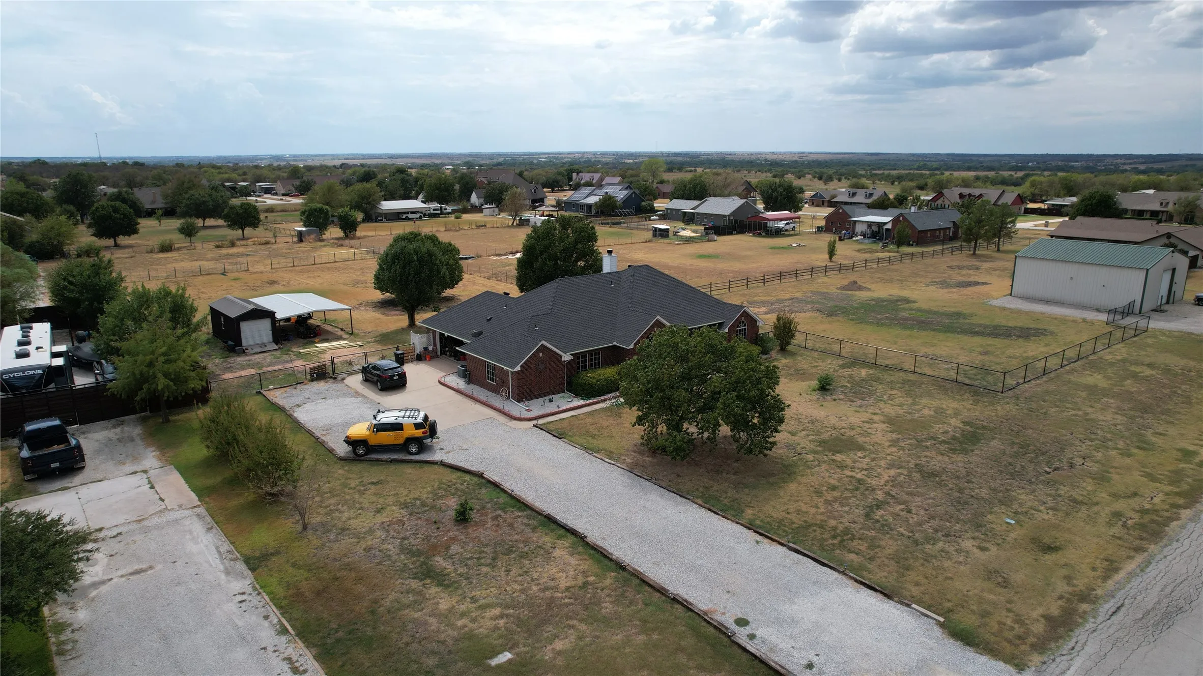 Brick exterior residence with an attached garage, paved driveway, detached metal outbuilding, and fenced property perimeter