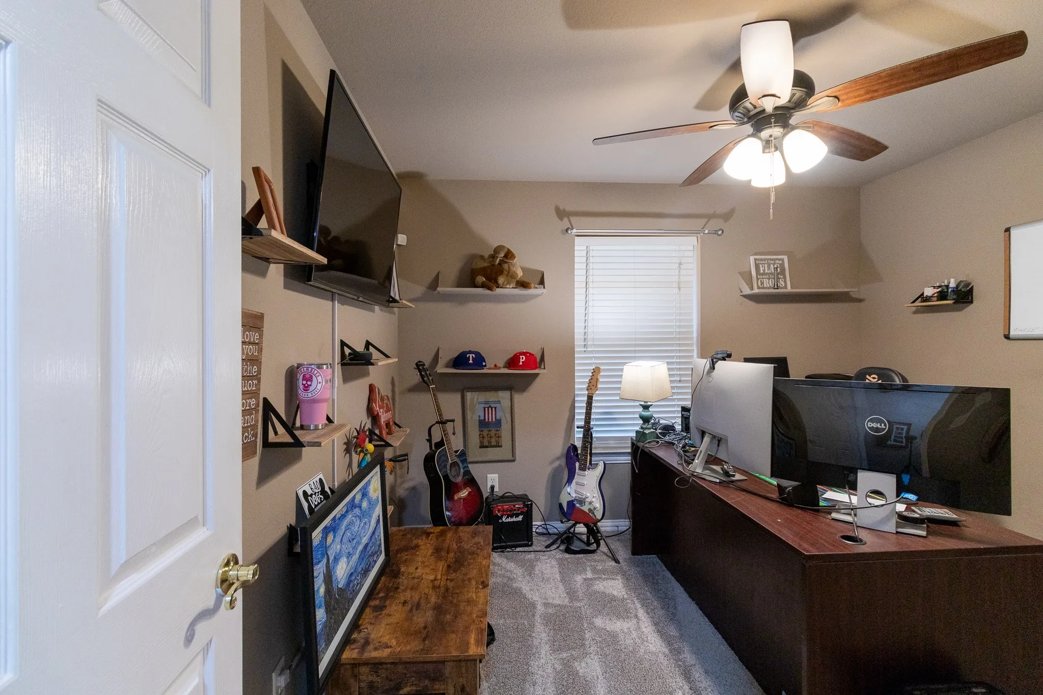 Wall-mounted shelving, wood-finish ceiling fan with light fixture, window with blinds, and neutral wall paint