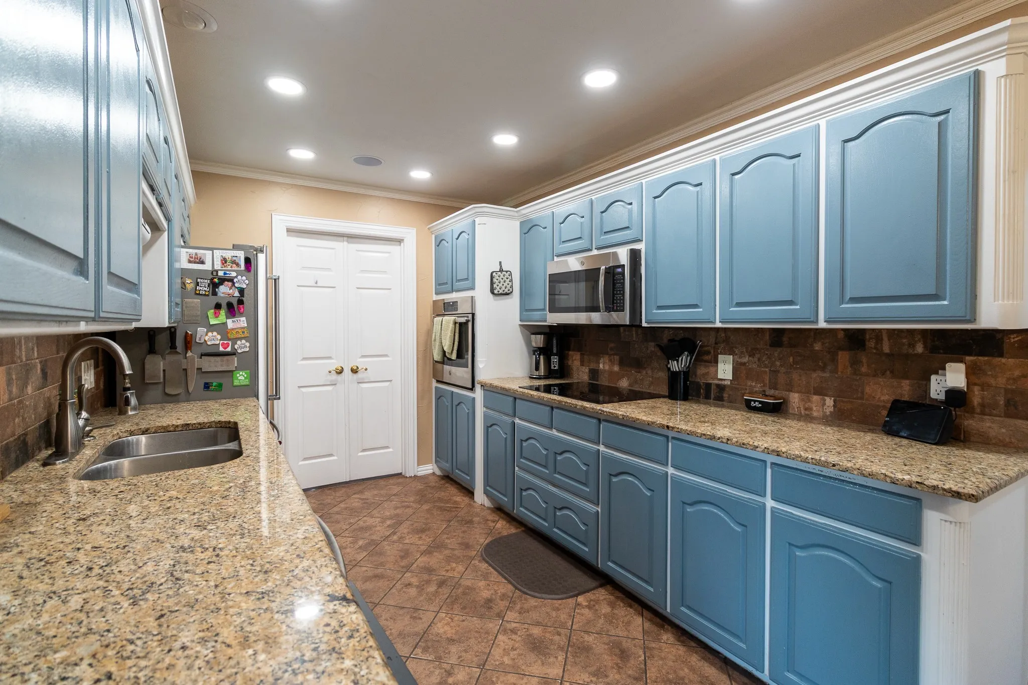 Kitchen featuring blue cabinetry, granite countertops, a stainless steel double sink, stainless steel appliances, and a tiled backsplash