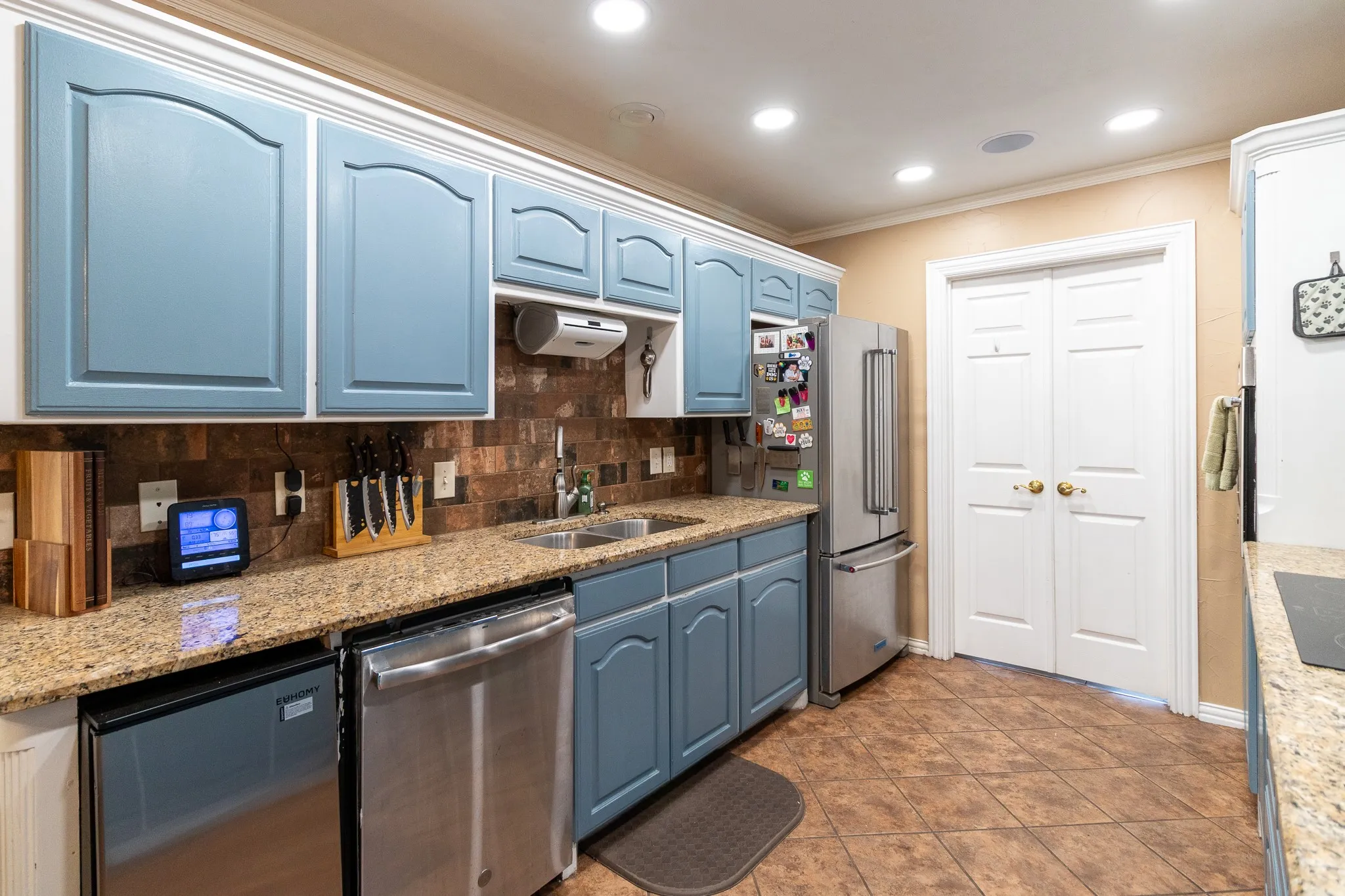 Recessed lighting, light-toned wall paint, two-tone cabinetry with upper white and lower blue finishes, granite countertops, and stainless steel appliances