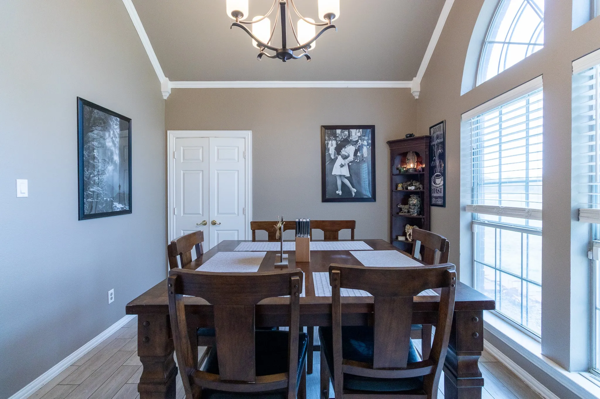 Tray ceiling with crown molding, arched window with horizontal blinds, wood-finish flooring, and double panel doors