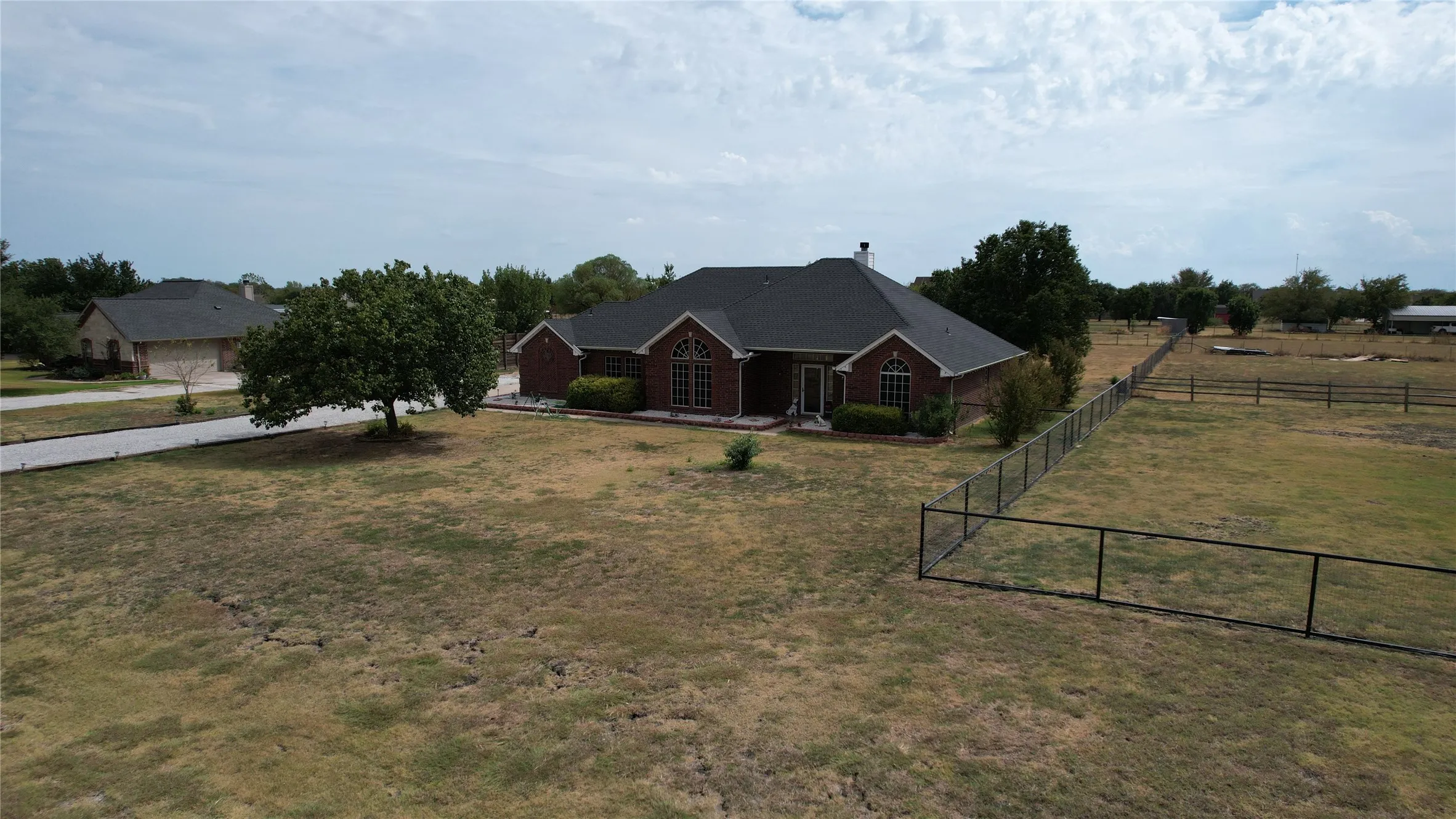 Brick exterior with dark roof, established tree, and paved driveway