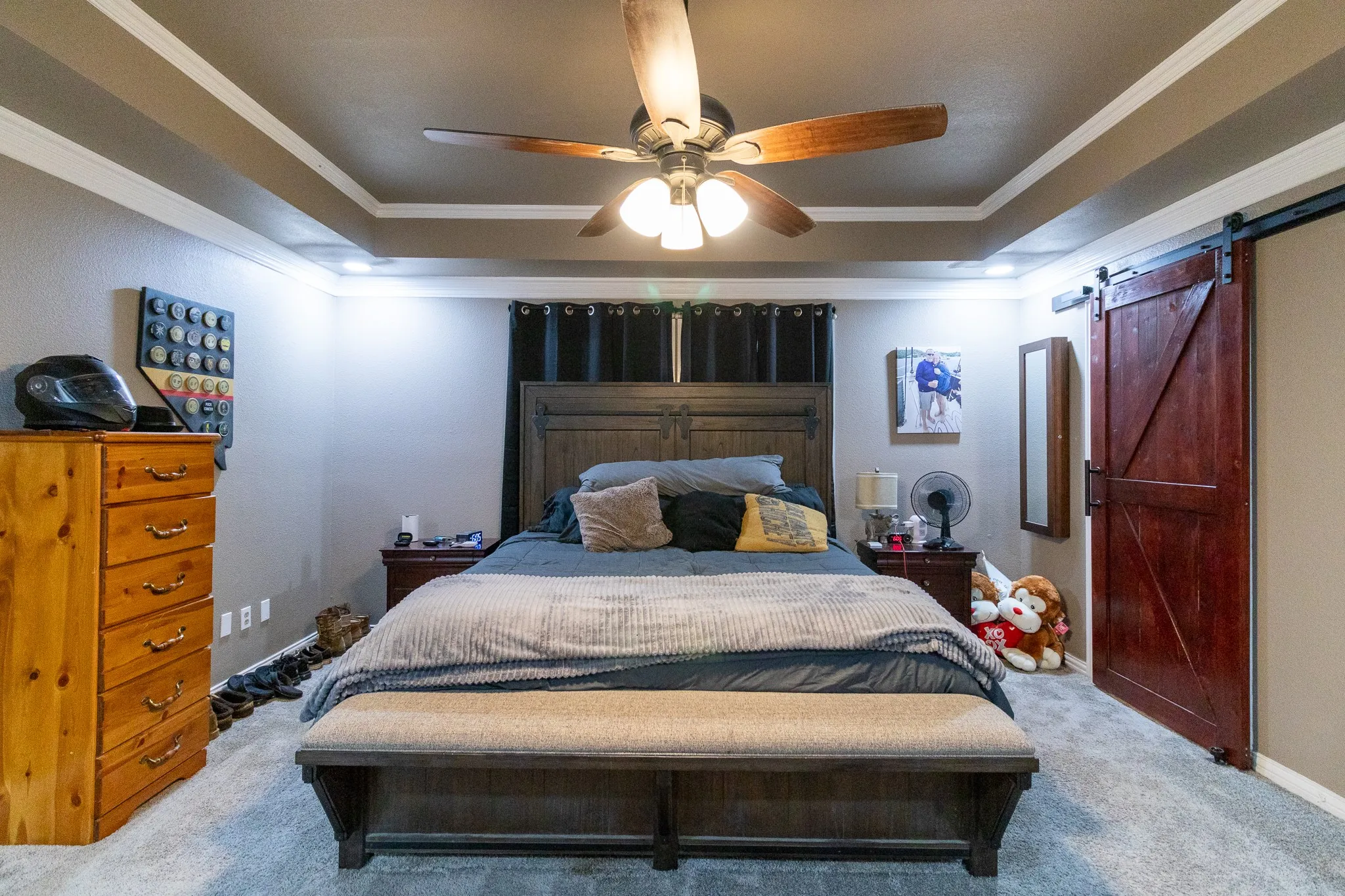 Tray ceiling with crown molding, recessed lighting, ceiling fan, carpet flooring, and a sliding barn door